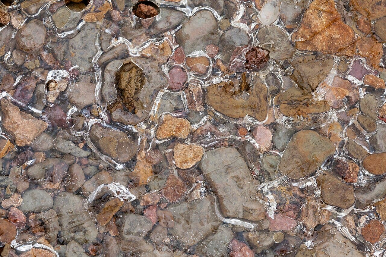 Clear ice formed over smooth brown and gray stones along the shoreline of Monroe Lake in Monroe County, Indiana