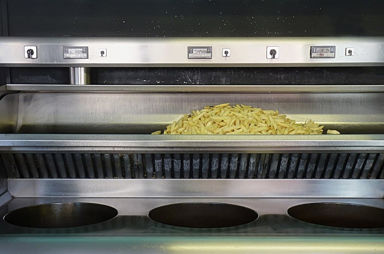 A commercial fryer station with a basket of fries and stainless-steel oil vats, one of the largest single sources of fats, oils, and grease in any kitchen