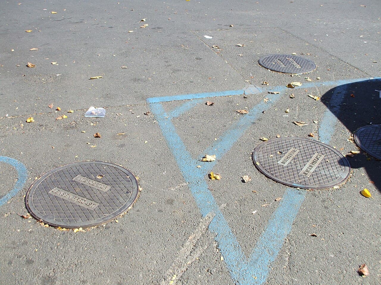 Two in-ground grease interceptor access lids cast with the word Interceptor in a commercial parking lot, with utility locating paint marks around them
