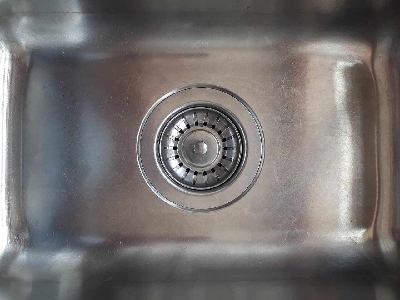 A close-up of a stainless-steel basket strainer seated in a commercial kitchen sink drain, catching food solids before they reach the grease trap